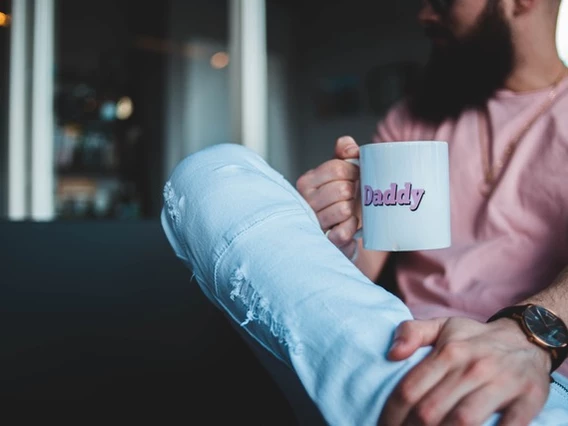 A man sits on a couch holding a mug that says daddy